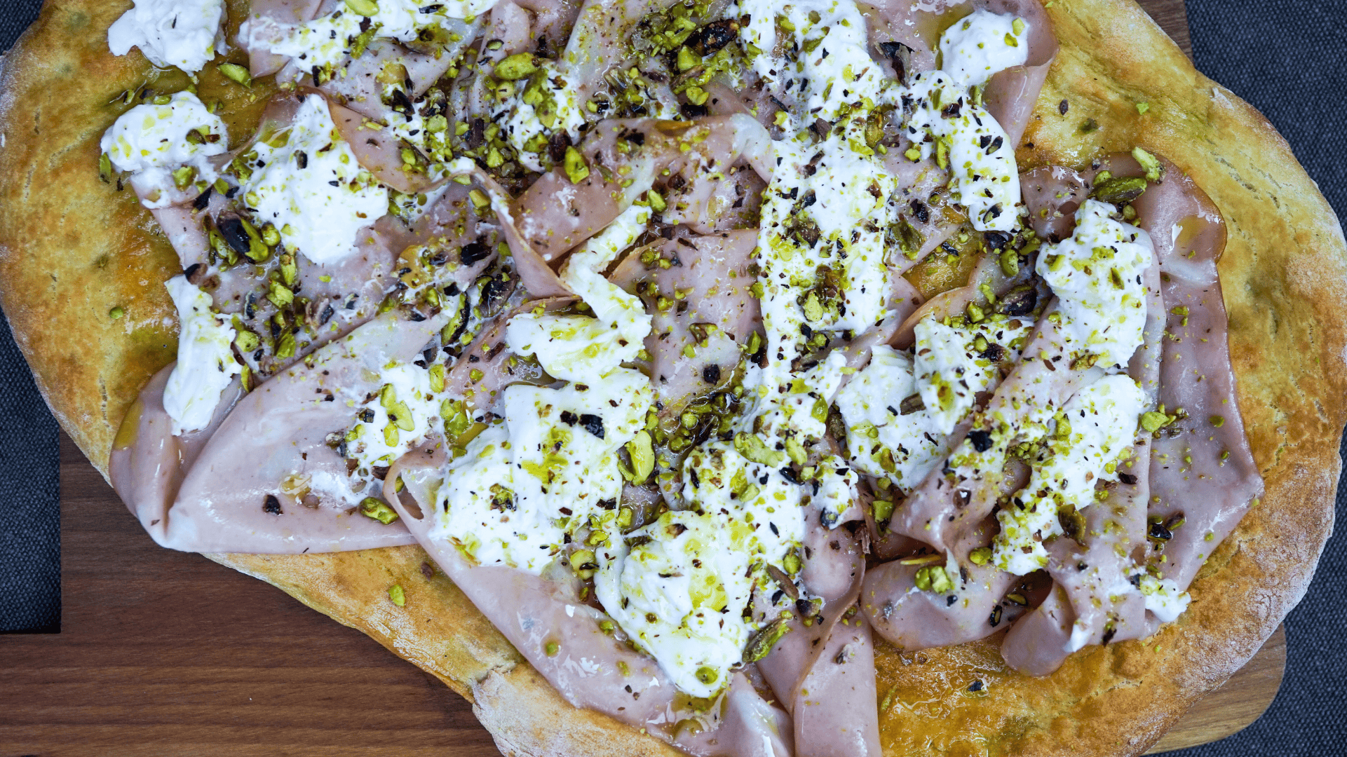 Crispy pizza with burrata, mortadella, chopped pistachios, and a drizzle of olive oil.