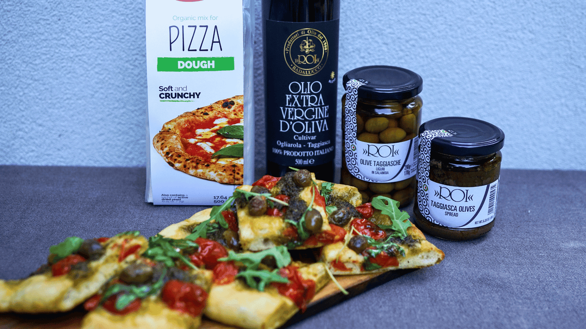 Homemade vegan pizza topped with cherry tomatoes, Taggiasca olives, vegan pesto, and fresh arugula