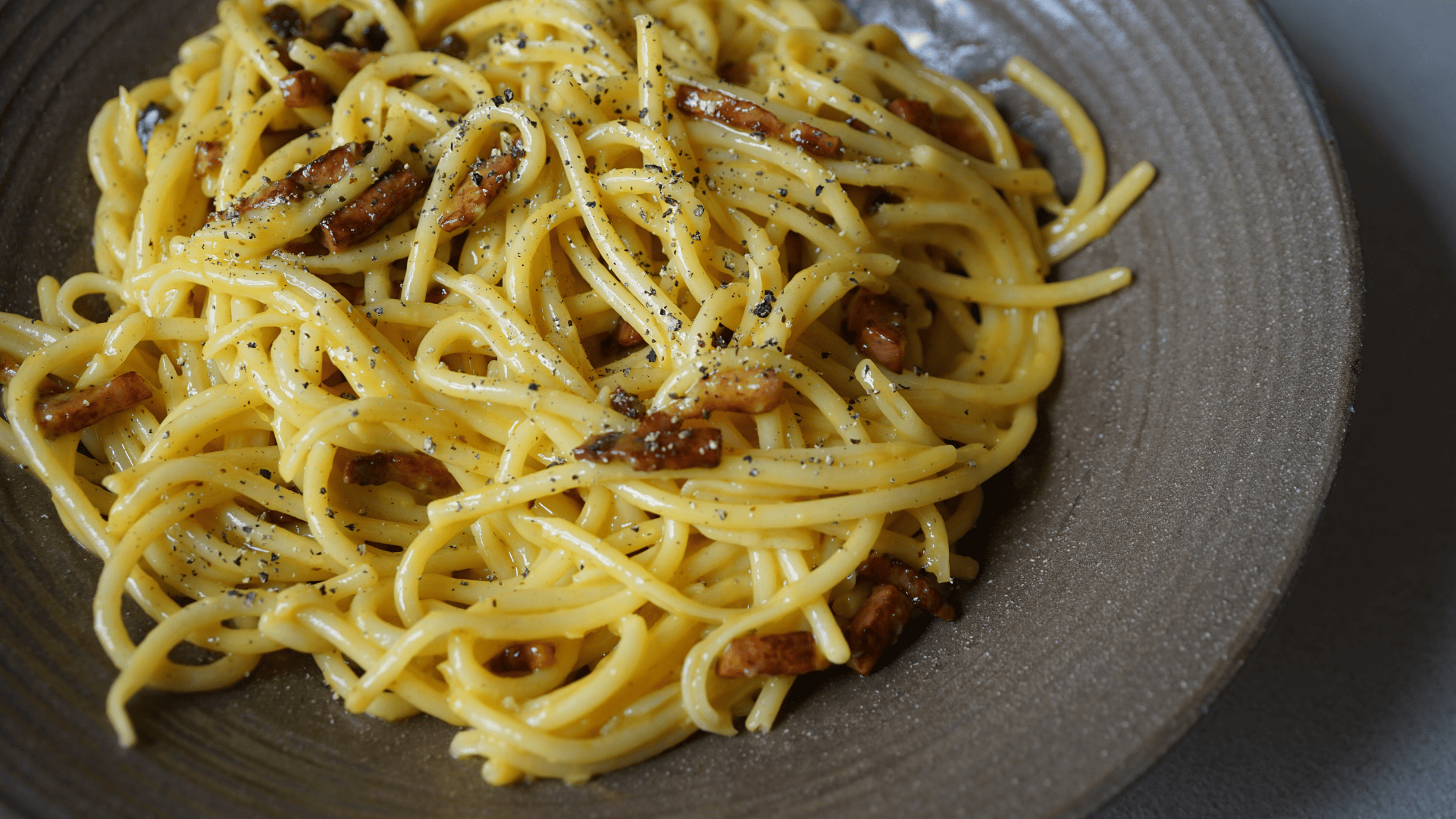 Bacon Carbonara with bucatini, crispy bacon, pecorino, parmigiano, and a creamy egg-based sauce, served with black pepper and extra cheese