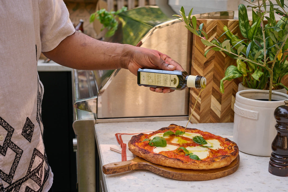 A close-up of a person drizzling high-quality Italian extra virgin olive oil over a freshly baked Margherita pizza