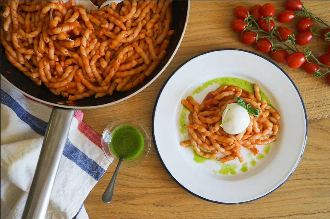Plated tomato and creamy burrata pasta with vibrant green basil oil drizzle.