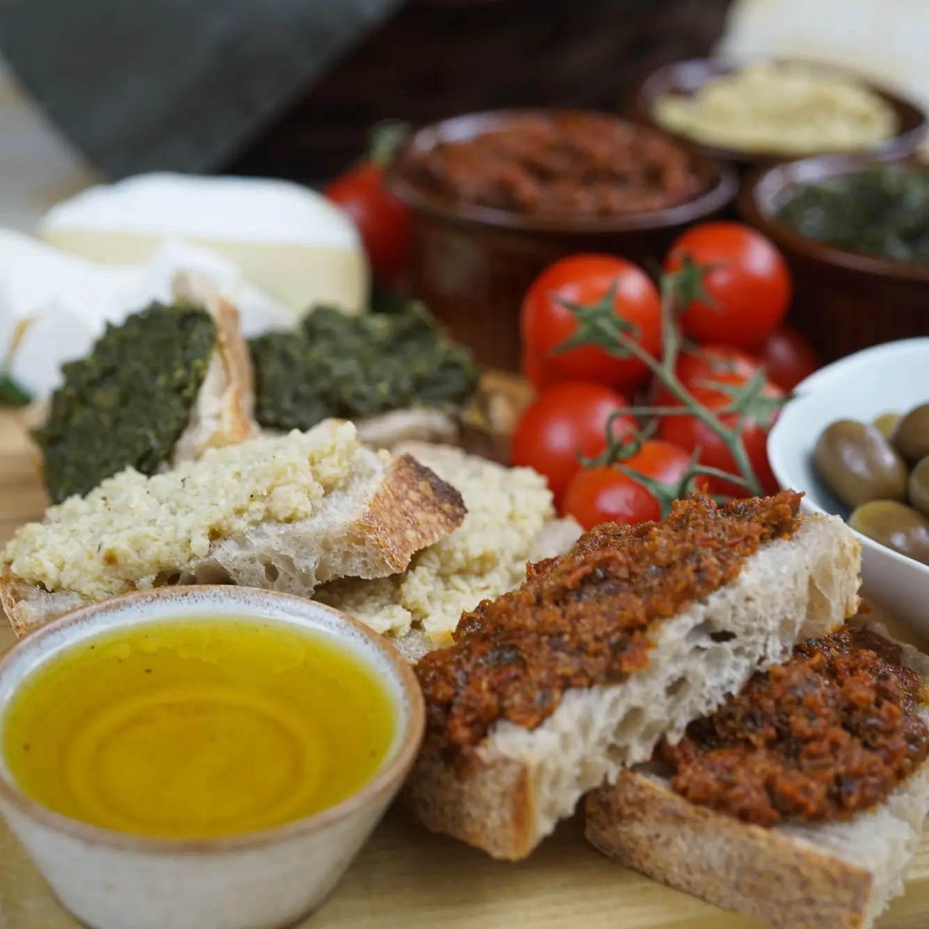 Platter of bread, olives, and tomatoes with a bowl of oil on a wooden surface.