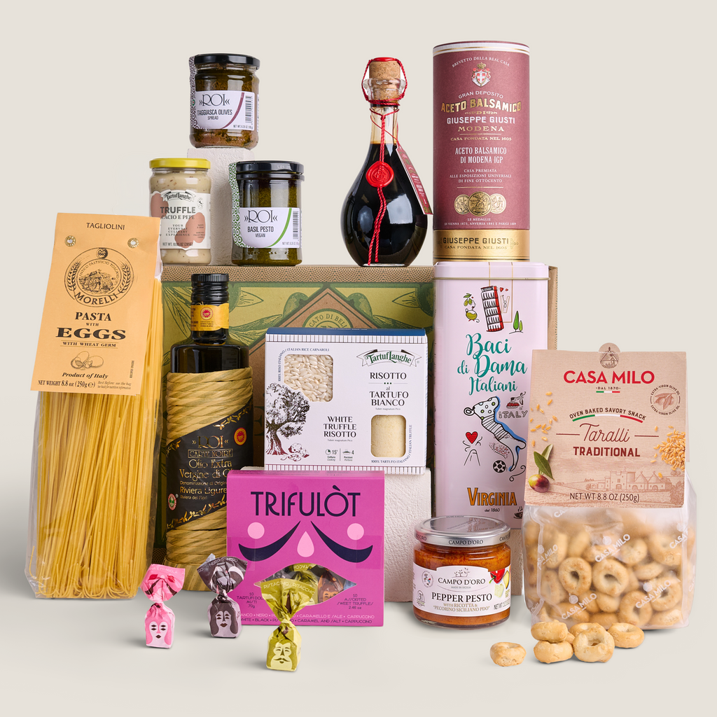 A curated gourmet gift hamper featuring an assortment of Italian products including pasta, chocolates, cheeses, crackers, and wine accessories, arranged neatly on a solid light beige background.