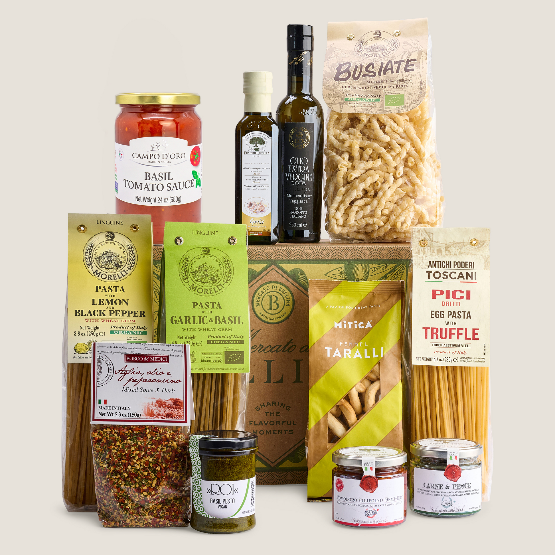 A curated gourmet food gift set featuring pasta, sauces, olive oil, and spices from multiple brands, arranged neatly on a light beige background.