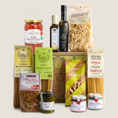 A curated gourmet food gift set featuring pasta, sauces, olive oil, and spices from multiple brands, arranged neatly on a light beige background.