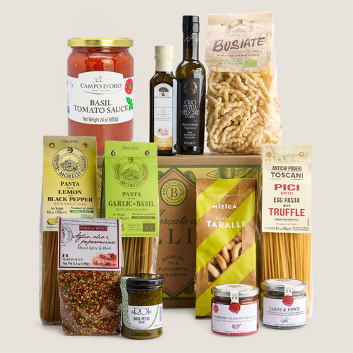 A curated gourmet food gift set featuring pasta, sauces, olive oil, and spices from multiple brands, arranged neatly on a light beige background.