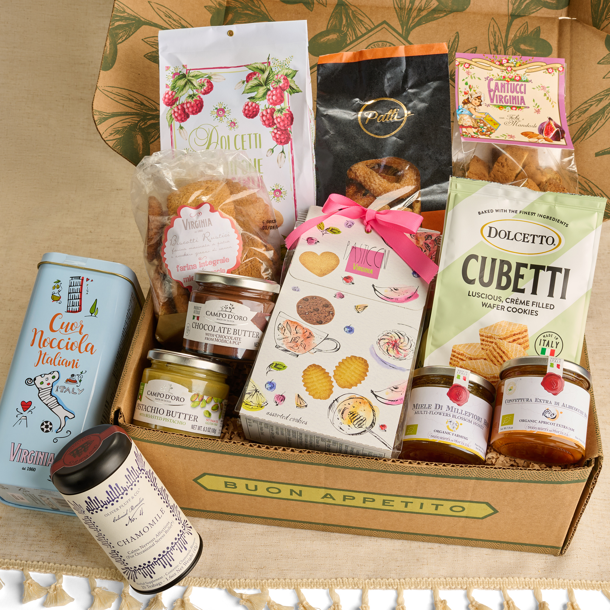Gourmet gift box with various food items including cookies, butter, and jam on a patterned surface.