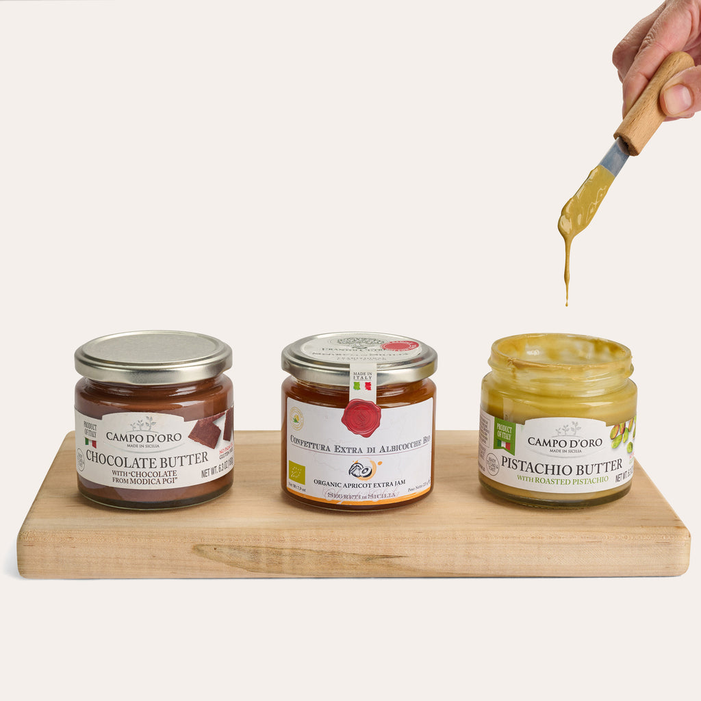 Jars of chocolate butter, apricot jam, and pistachio butter on wooden board