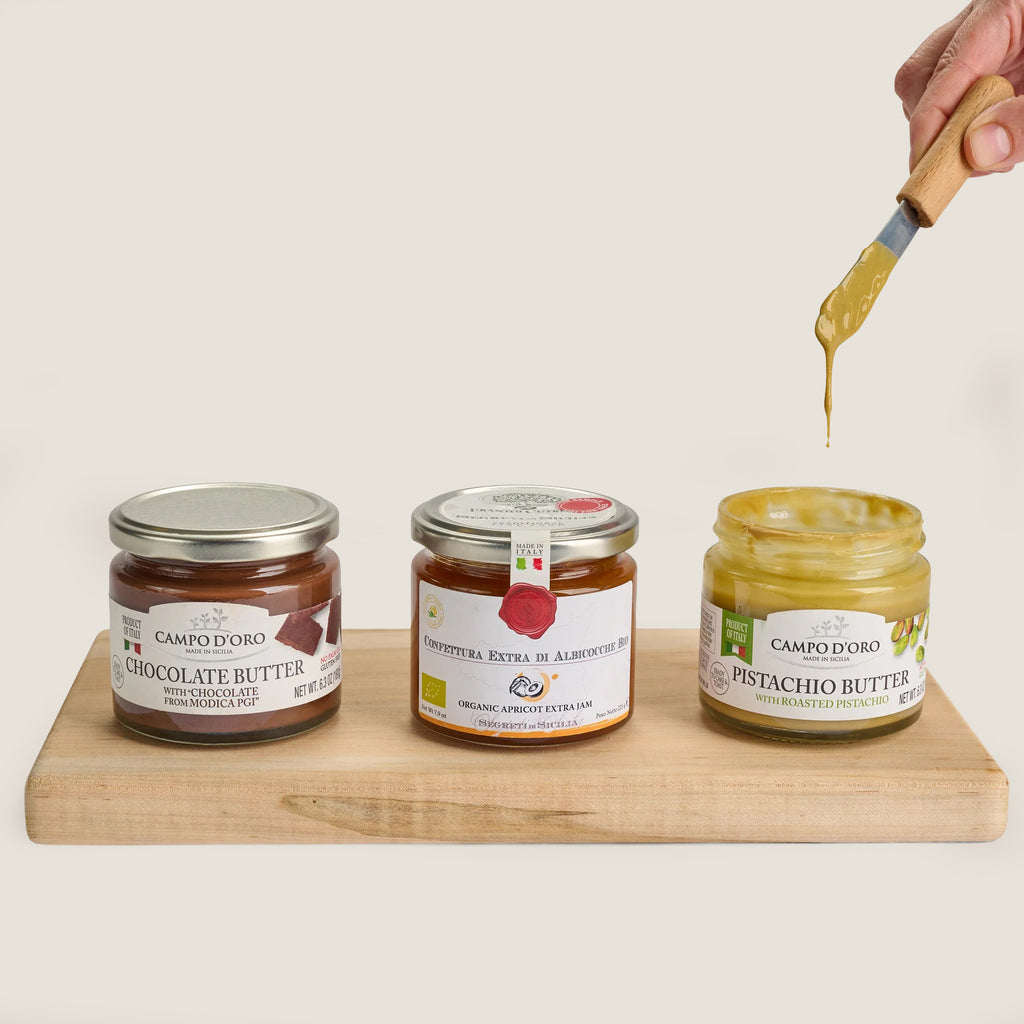Jars of chocolate butter, apricot jam, and pistachio butter on wooden board