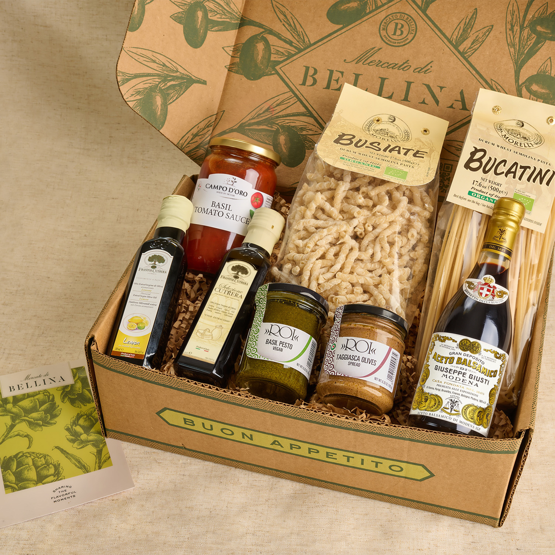 A gourmet gift box from Buon Appetito by Mercato di Bellina, filled with various Italian delicacies including pasta, sauces, and spreads, set on a neutral beige background.