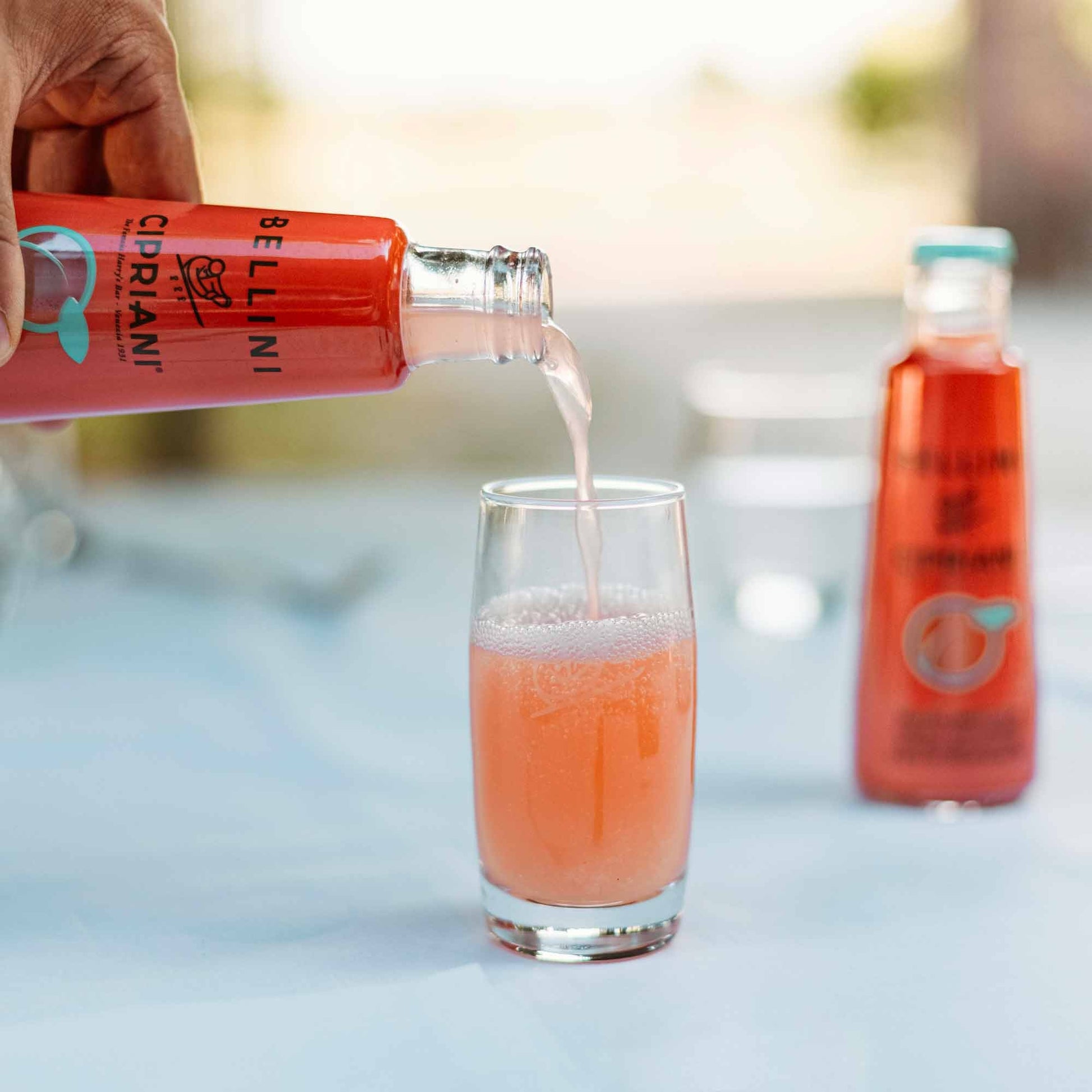Hand pouring Cipriani Bellini peach cocktail drink into glass