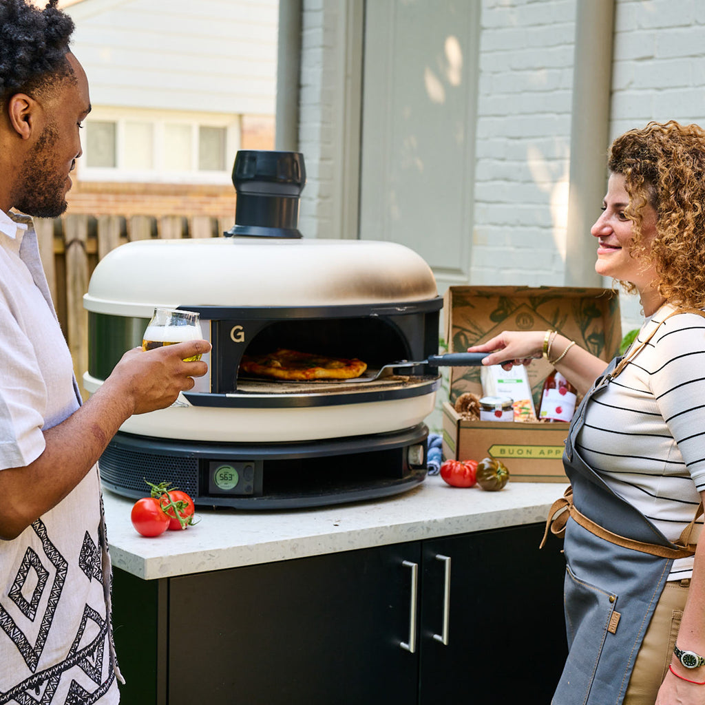 Woman baking homemade pizza in outdoor oven with Italian toppings
