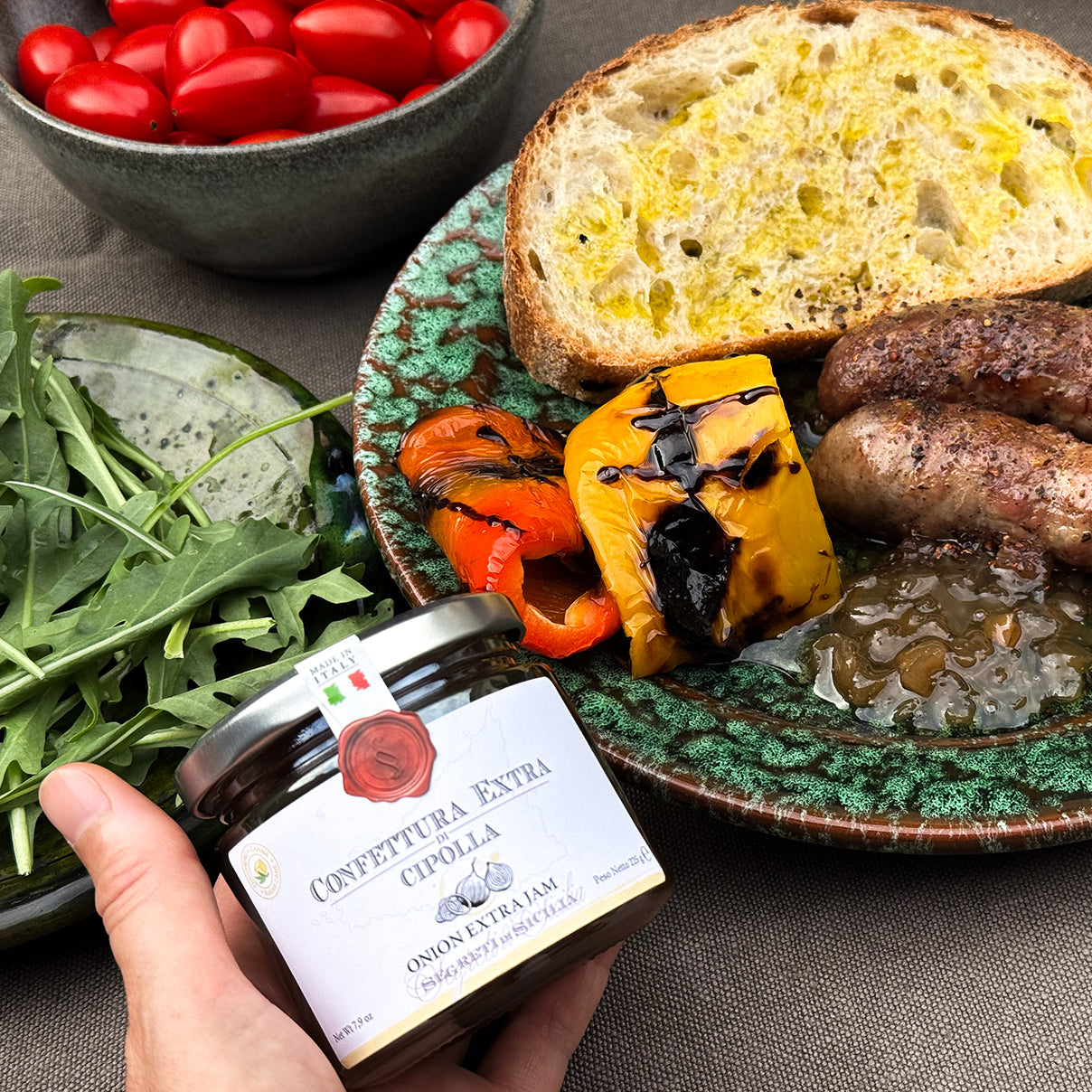 Onion jam with roasted peppers, sausage, and rustic bread on a green ceramic plate