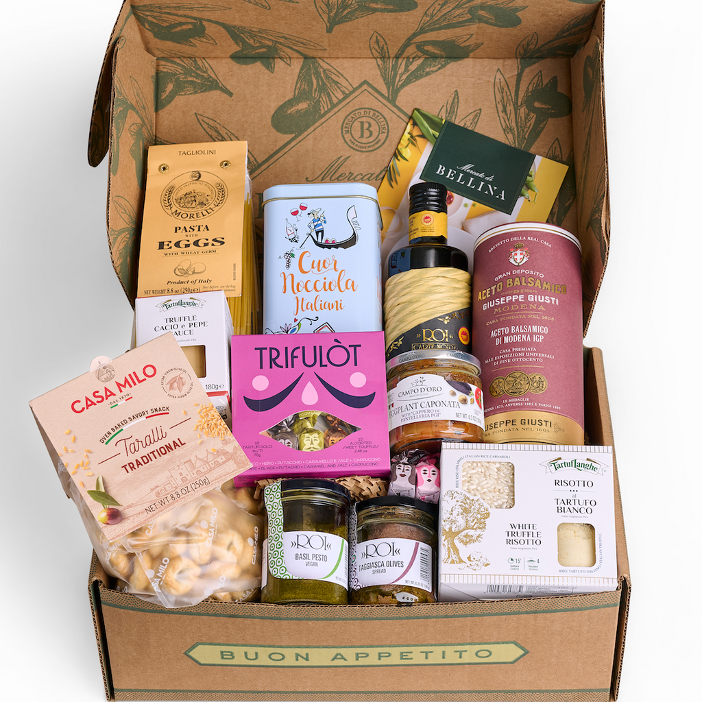 A curated gourmet gift box from Buon Appetito, filled with an assortment of Italian snacks, cheeses, chocolates, and wines. Visible items include a box of Trifulot chocolates, Bellina Prosecco, Casa Milano Truffle, and various other packaged food products arranged inside a brown cardboard box with green botanical illustrations.
