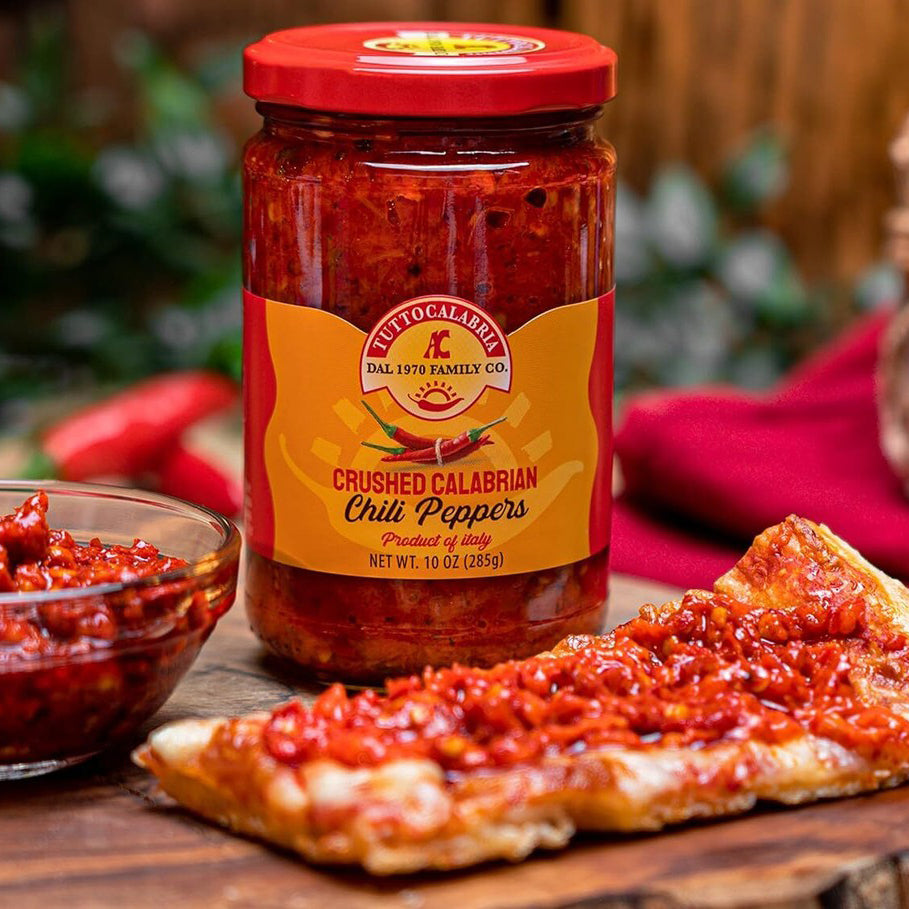 Jar of Tutto Calabria crushed Calabrian chili peppers beside pizza and bowl